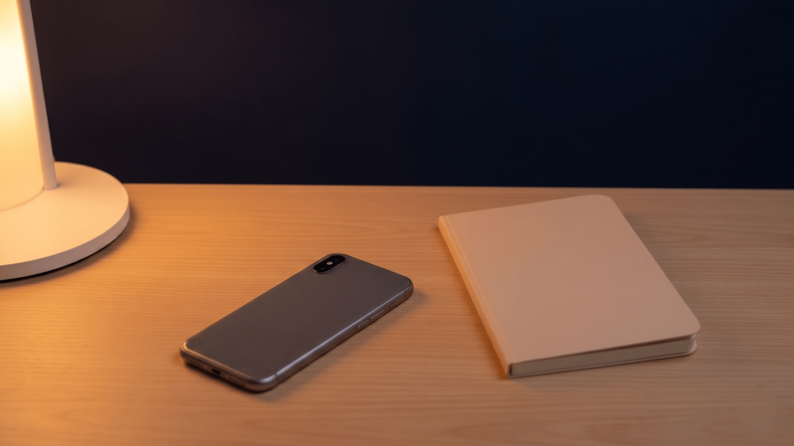 Smartphone and notebook on a wooden desk illuminated by a lamp